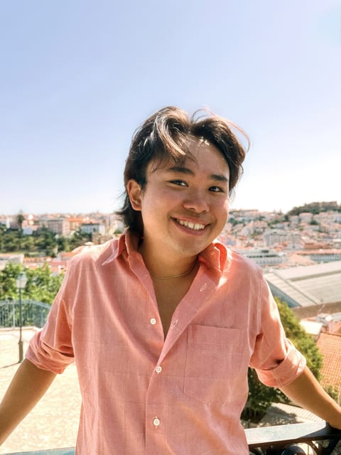 Patrick H. Pan smiling in a coral shirt, red roofs and a blue sky behind him